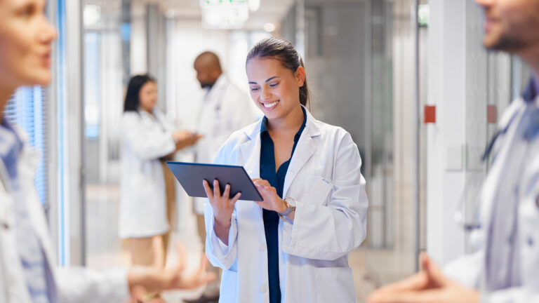 Doctor holding and looking at a tablet in a medical clinic, smiling while surrounded by colleagues