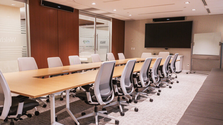 An empty Welch LLP conference room with a long table and dozens of chairs.