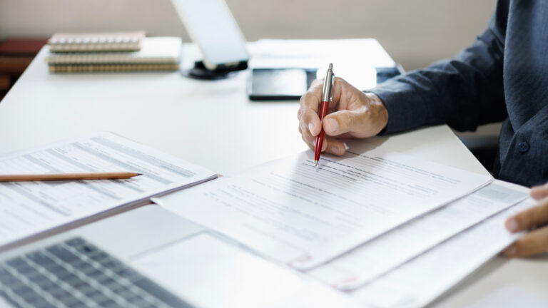 A man in a blazer holds a pen as he reads through a new form to be filled out