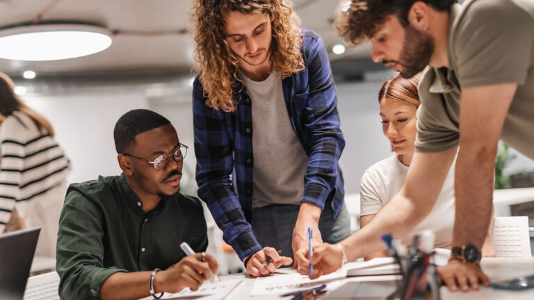 A group of young adults gather around a table as they review paperwork anf forms on a table.